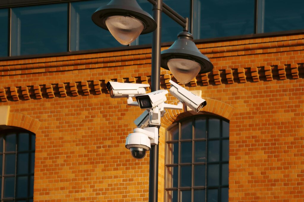 Modern security cameras mounted on a pole against a brick building in the city.