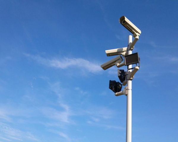 Multiple security cameras on a pole with a clear blue sky backdrop.