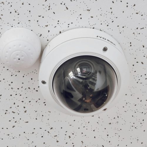 Close-up of a round dome surveillance camera installed on a speckled ceiling for security monitoring.